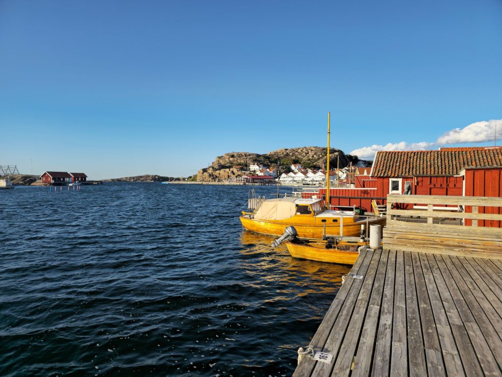 Wooden boats tied up beside a red boathouse and jetty in Hunnebostrand harbour.