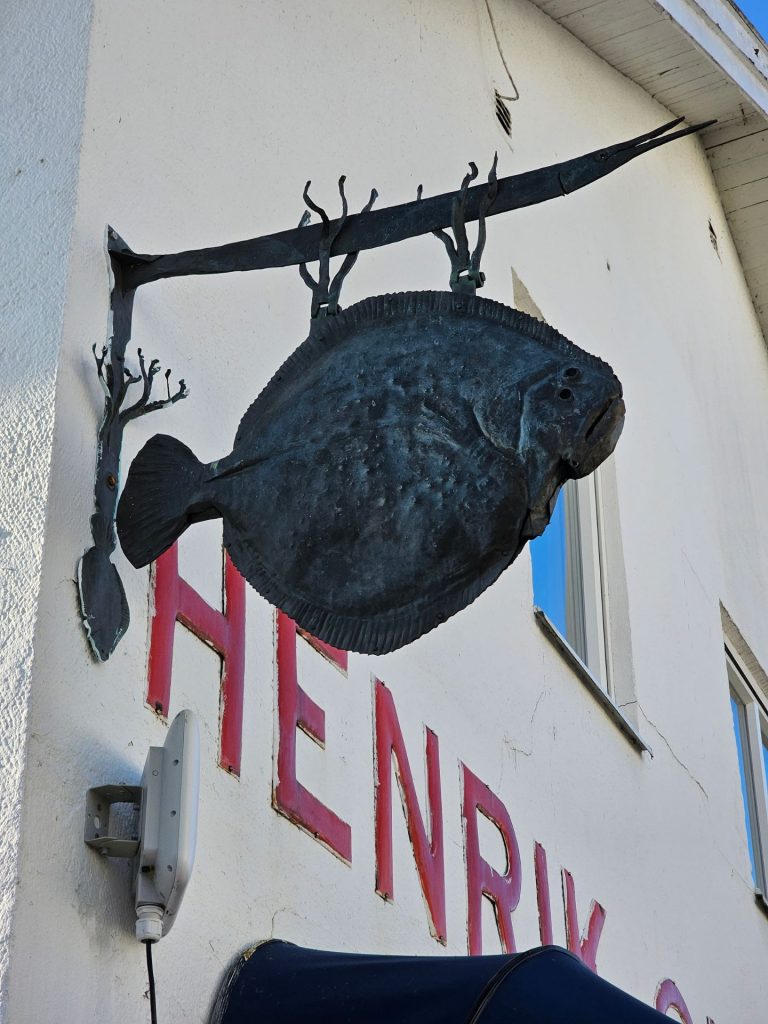 Hanging fish-shaped sign on the facade of Henriks Sjökrog seafood restaurant in Hunnebostrand.